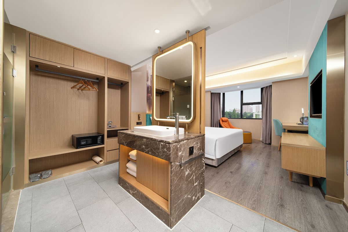 A modern hotel room with a marble bathroom vanity, a bed, a desk, and a view of the city.