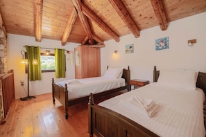 Una habitación con vigas de madera, dos camas, un armario, una lámpara y una ventana con cortinas.