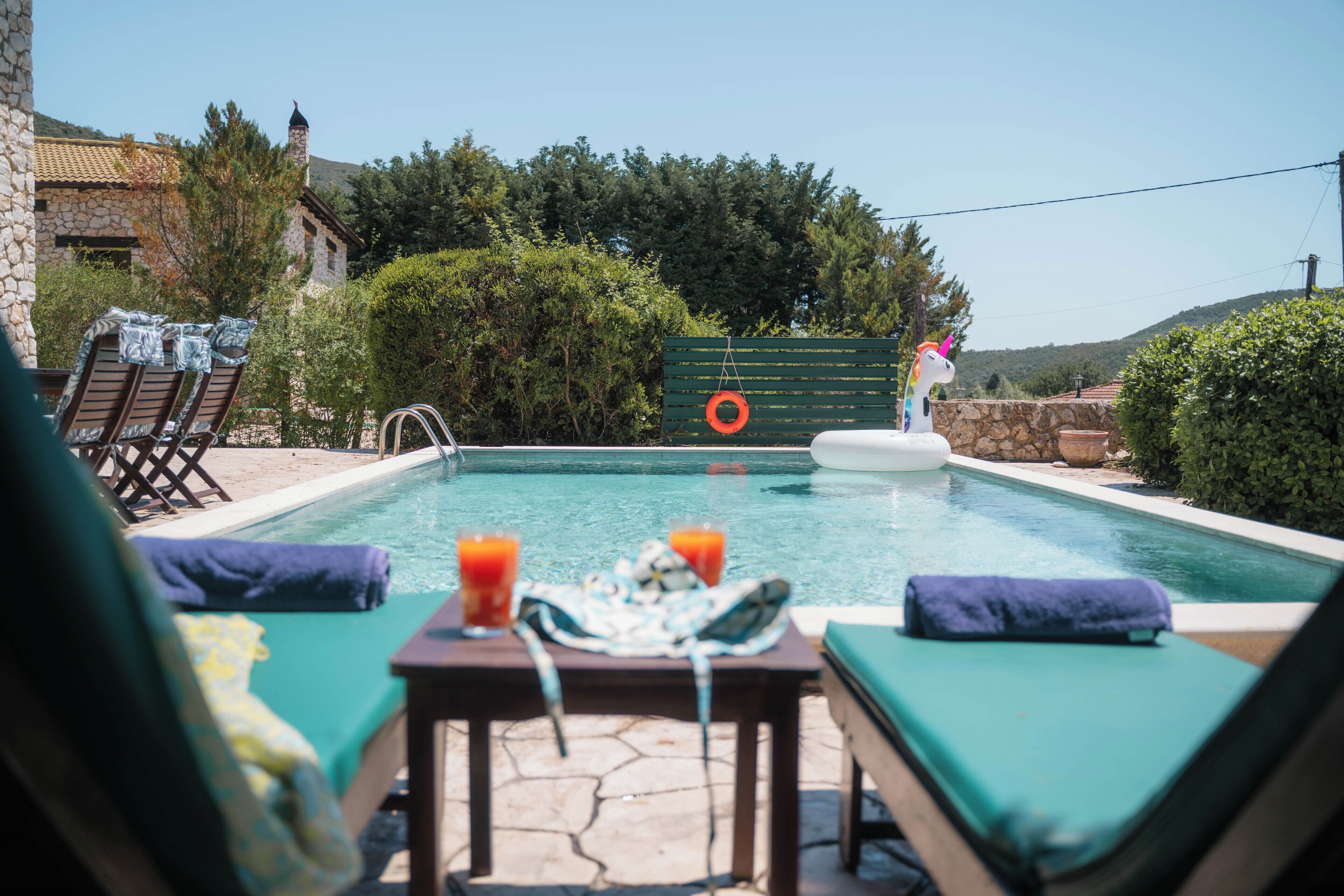 Zona de piscina amb gandules, una taula amb begudes i un flotador.