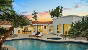 A swimming pool with lounge chairs, a patio area, and a building with large windows. - SWSS 8BR Palms Away Estate | Pool, Hot Tub, Sport Court, Putting Green & Games (Scottsdale)