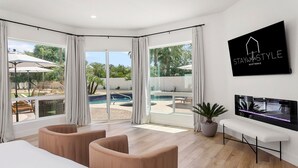 A modern bedroom with a large window, a TV, and a potted plant. - SWSS 8BR Palms Away Estate | Pool, Hot Tub, Sport Court, Putting Green & Games (Scottsdale)