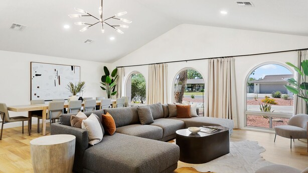 A modern living room with a sectional sofa, round coffee table, and a dining area with a whiteboard. - SWSS 8BR Palms Away Estate | Pool, Hot Tub, Sport Court, Putting Green & Games (Scottsdale)