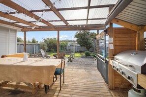 Un patio couvert avec un barbecue, une terrasse en bois et un espace salon extérieur.