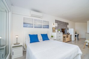 A modern bedroom with a large bed, bedside tables, a desk, and a kitchenette.