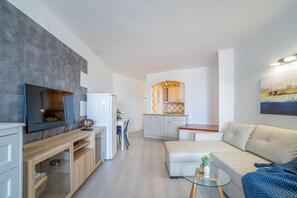 A modern living room with a flat-screen TV, a glass coffee table, and a beige sofa.