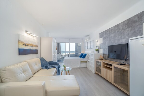 A modern, well-lit living room with a sofa, a glass coffee table, and a TV on a wooden cabinet.