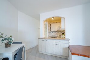 A compact kitchen with white cabinets, a small dining area with a table and chairs, and a tiled backsplash.