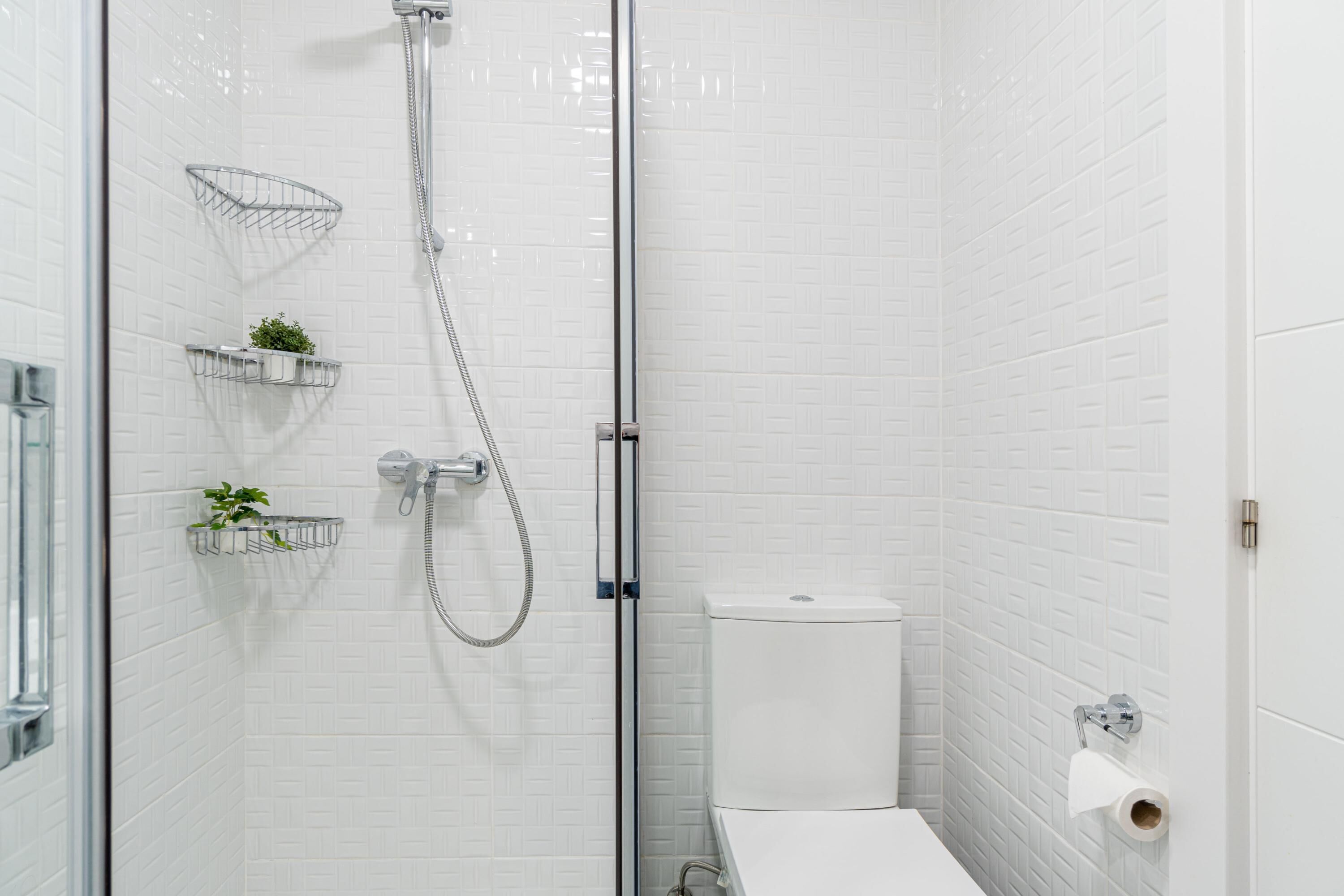 A modern bathroom with white subway tiles, a glass shower enclosure, a toilet, and two small plant baskets on the wall.