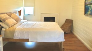 Een slaapkamer met een bed, een open haard, een raam en een schilderij aan de muur.