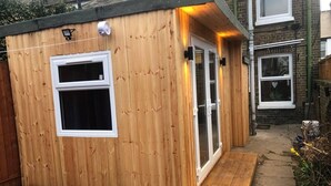 A wooden shed with a single window and a door, a small wooden ramp leading to the entrance, and a brick wall in the background. - Two Bedroom House, Birchington, ct79rn (Birchington)