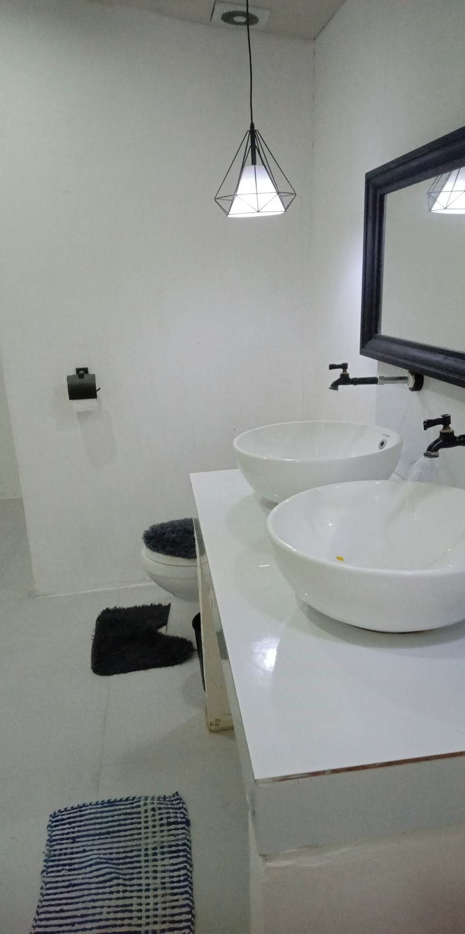 Une salle de bain avec deux lavabos blancs, un miroir noir et un luminaire suspendu aux formes géométriques.