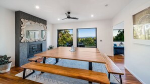 A modern dining area with a wooden table and benches, a decorative mirror, and a fireplace.