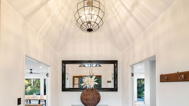 A hallway with a high ceiling, a large mirror, a decorative vase, and a console table.