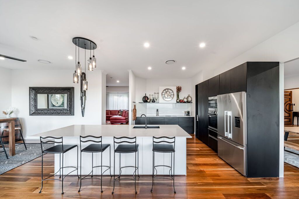 A modern kitchen with a central island, bar stools, a stainless steel refrigerator, and a pendant light fixture.
