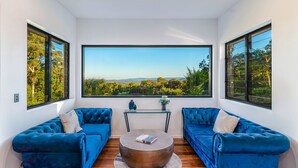 A room with two blue sofas, a round coffee table, and large windows offering a view of greenery and hills.