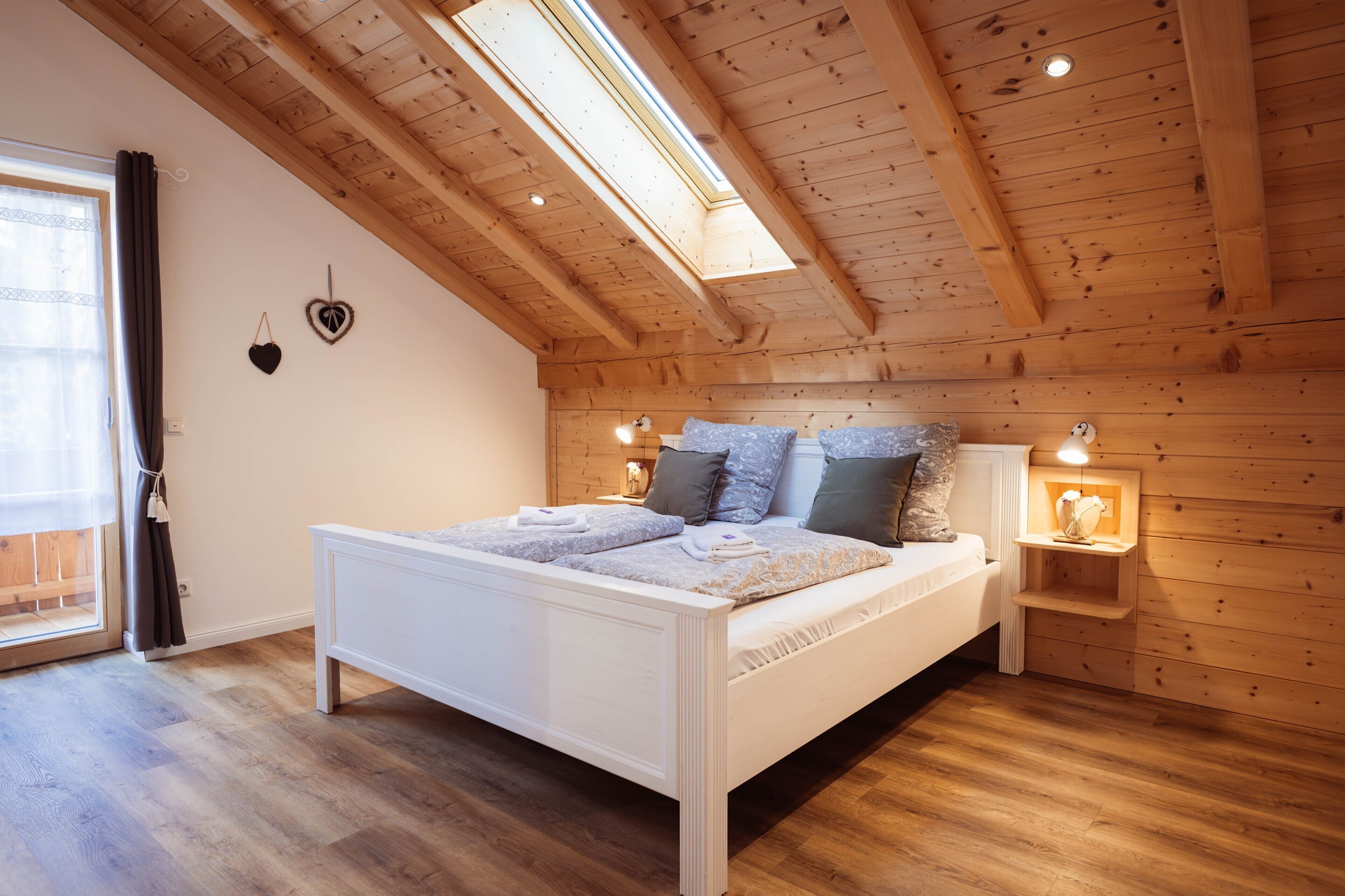 A bedroom with a wooden ceiling, a bed with patterned bedding, and a nightstand with a lamp.