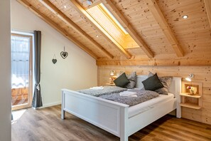 A bedroom with a sloped ceiling, a bed with patterned bedding, bedside lamps, and a small shelf with a flower. - Apartment "Brauneck" with Mountain View, Balcony and Wi-Fi (Gaißach)