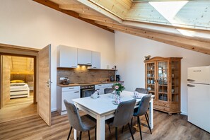 A compact kitchen with wooden cabinets, a dining table with chairs, a refrigerator, and a cabinet with glass doors. - Apartment "Brauneck" with Mountain View, Balcony and Wi-Fi (Gaißach)