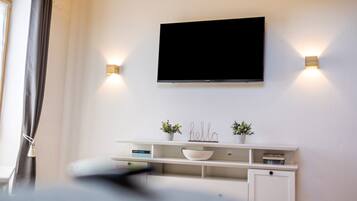 Ein modernes Zimmer mit einem Wand-Fernseher, einem weißen Konsolentisch mit Dekoration und zwei Wandleuchten.