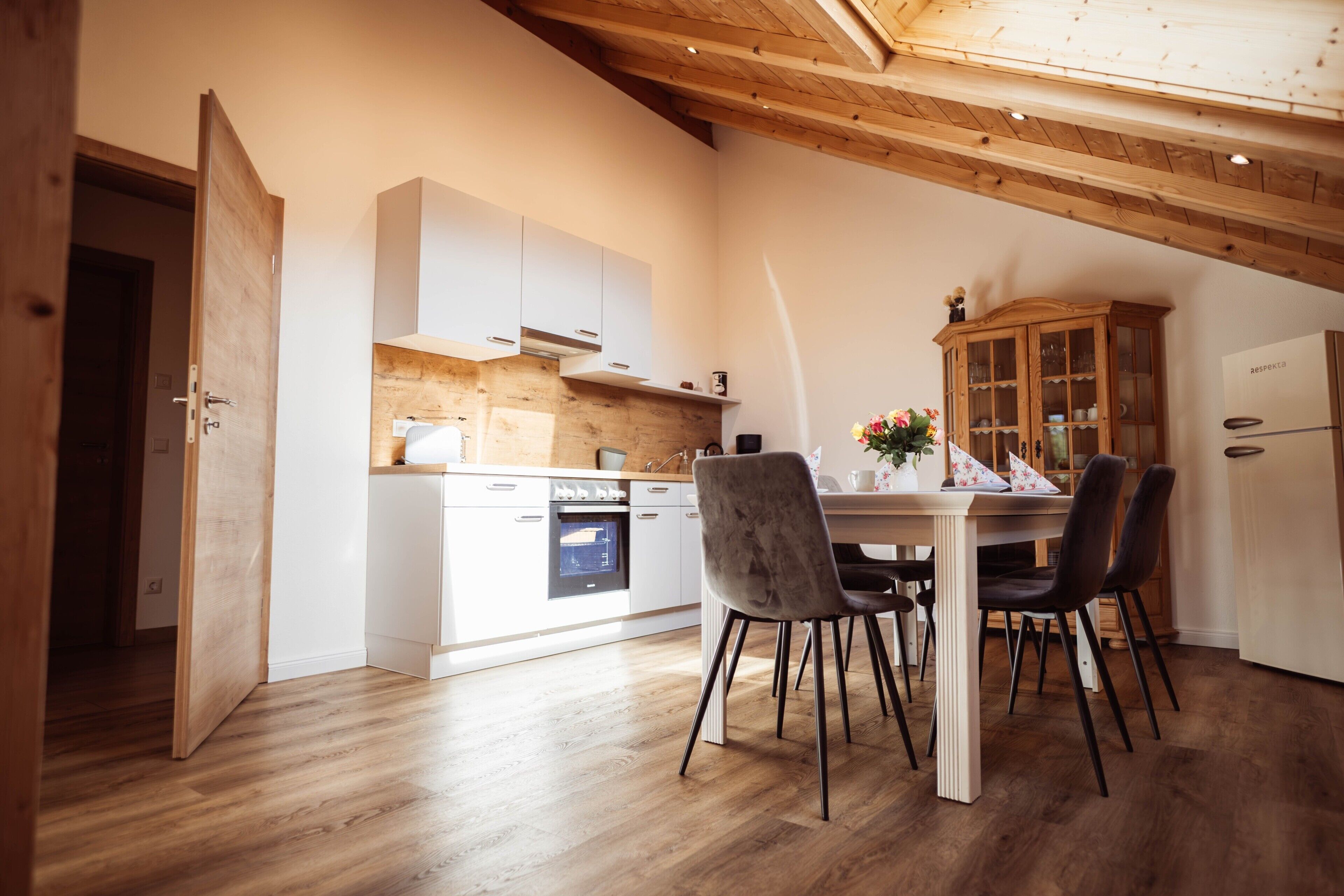 A modern kitchen with white cabinetry, a wooden ceiling, and a dining area with a table and chairs.