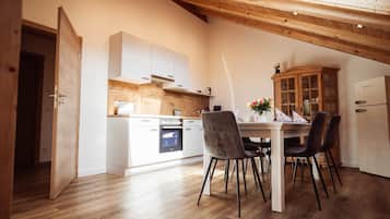 A modern kitchen with white cabinetry, a wooden ceiling, and a dining area with a table and chairs.