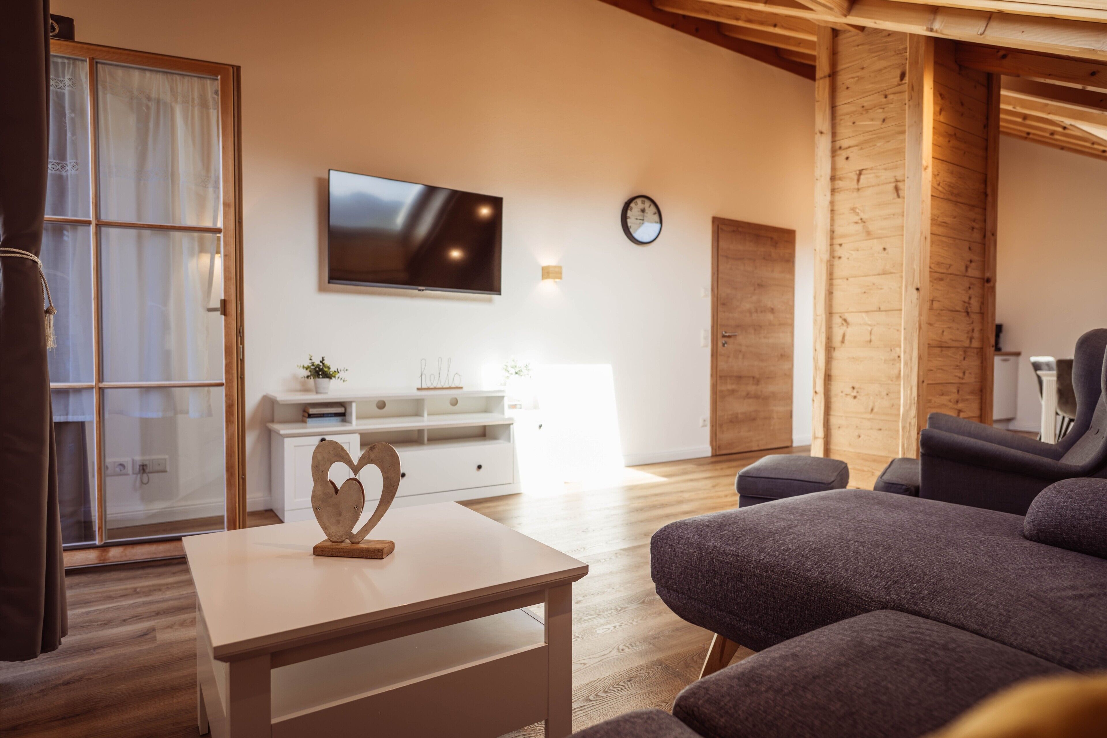 Un soggiorno moderno con una televisione a schermo piatto, un soffitto in legno, un divano e un tavolino con un cuore decorativo.