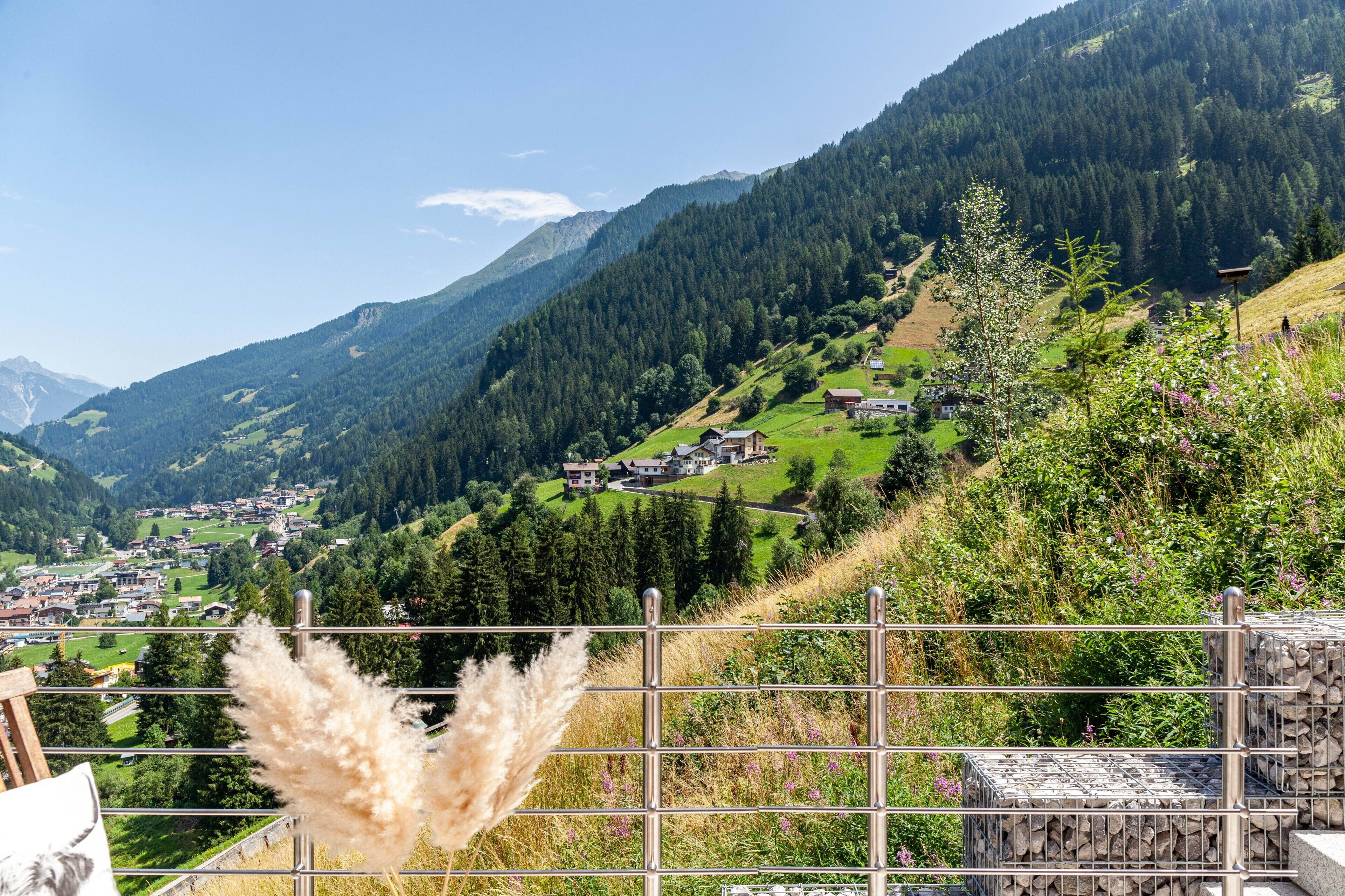 A mountainous landscape with a village, a metal fence, and pampas grass.