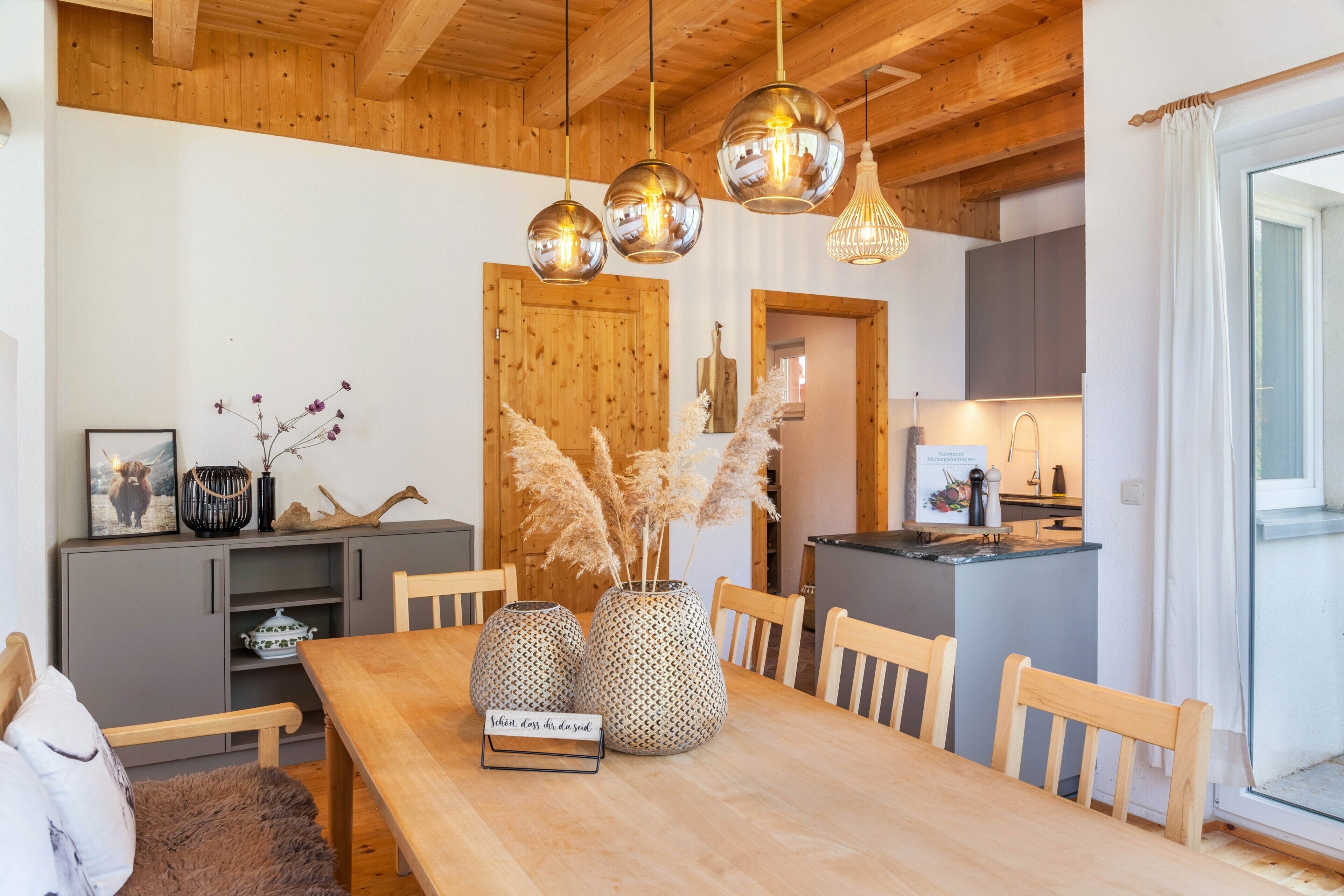 A wooden dining table with three spherical vases, a wooden bench, and a kitchen area with a wooden door and cabinets.