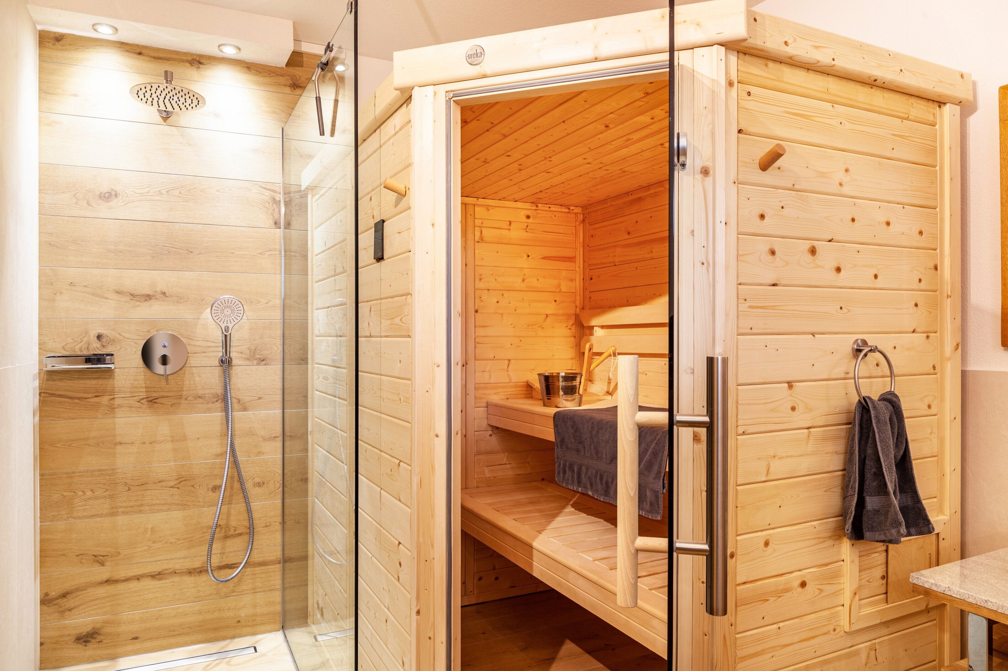A wooden sauna with a glass-enclosed shower, a bench, and towels.