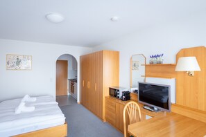 Habitación de hotel con cama, escritorio con televisor, microondas, lámpara y mueble pequeño.