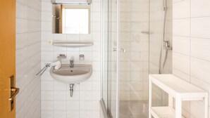 A bathroom with a sink, mirror, shower, and shelving.