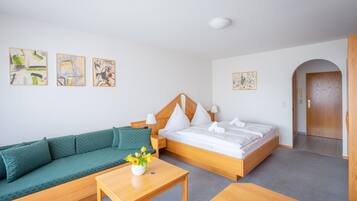 Hotelkamer met een bed, een groene bank, een houten tafel met een bloevas en kunstwerken aan de muur.