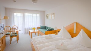 A hotel room with a bed, a sofa, a desk with a chair, a TV, and a window with curtains.