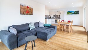 Een moderne woonkamer met een grijze modulaire bank, een klein rond tafeltje en een eethoek met houten stoelen.