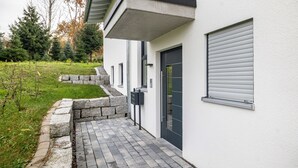 Een modern gebouw met een stenen pad dat leidt naar een deur, een overdekt gedeelte en een raam met zonwering.