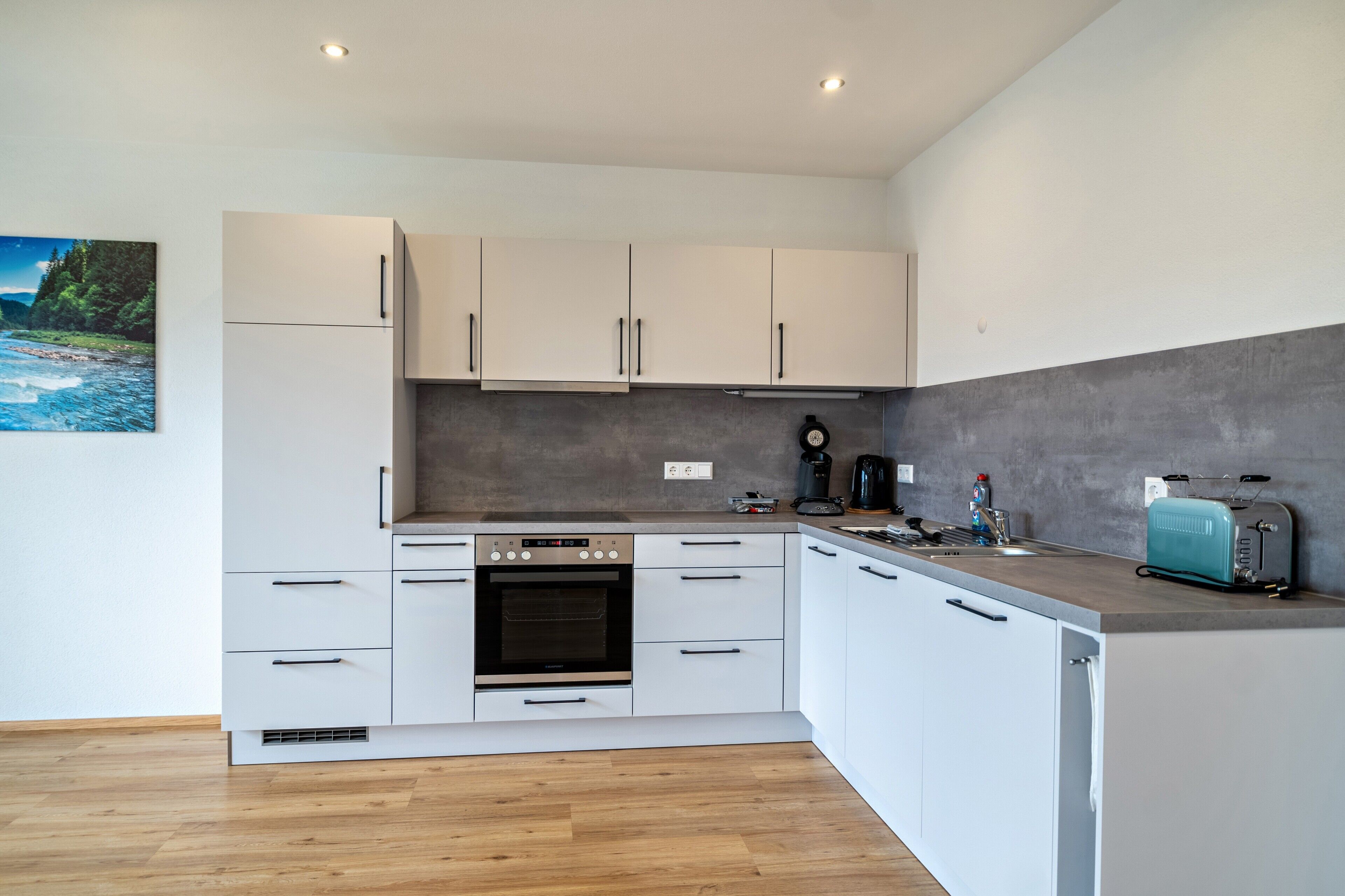 Una cocina moderna con armarios blancos, horno empotrado, cafetera y tostadora en la encimera.