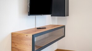 Een aan de muur bevestigde televisie op een houten consoles met een afstandsbediening.