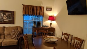 Comedor con mesa de madera, seis sillas, lámpara roja, cafetera y ventana con persianas.