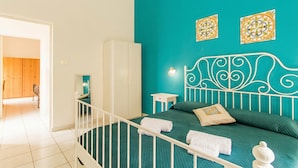A bedroom with a teal wall, a white metal headboard, a bed with green bedding, a white wardrobe, and two decorative wall pieces. - Sicula home in the city center, Catania, Italy (Catania)