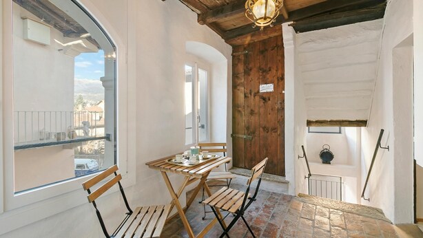 Una habitación con una mesa de madera para dos personas, un banco, una puerta de madera y una vista por una ventana.