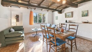 Un comedor con mesas y sillas de madera, un sofá y un ventanal con cortinas.