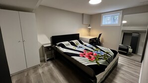 Ein Schlafzimmer mit einem Bett, einem Schreibtisch, einem Stuhl, einem Nachttisch, einem Kleiderschrank und einem Fenster.