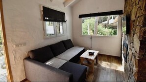 A cozy room with a sofa, a small table, a window with a view of greenery, and a stone wall.