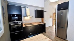 A modern kitchen with black cabinetry, a stainless steel refrigerator, and a built-in oven.