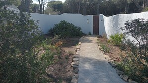 A pathway leading to a white-walled building with a wooden door, surrounded by greenery and trees. - House Palmito 2, Chiclana de la Frontera (Chiclana de la Frontera)