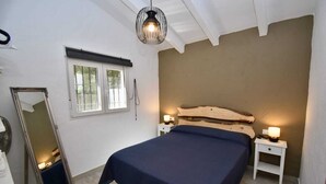 A bedroom with a large bed, two bedside tables with lamps, a mirror leaning against the wall, and a window with blinds. - House Palmito 2, Chiclana de la Frontera (Chiclana de la Frontera)