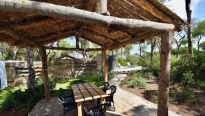 A wooden picnic table with chairs under a thatched roof structure in a garden setting. - House Palmito 2, Chiclana de la Frontera (Chiclana de la Frontera)