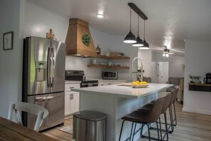 Una cocina moderna con un refrigerador de acero inoxidable, una campana extractora de madera, luces colgantes y una isla central con taburetes de bar.