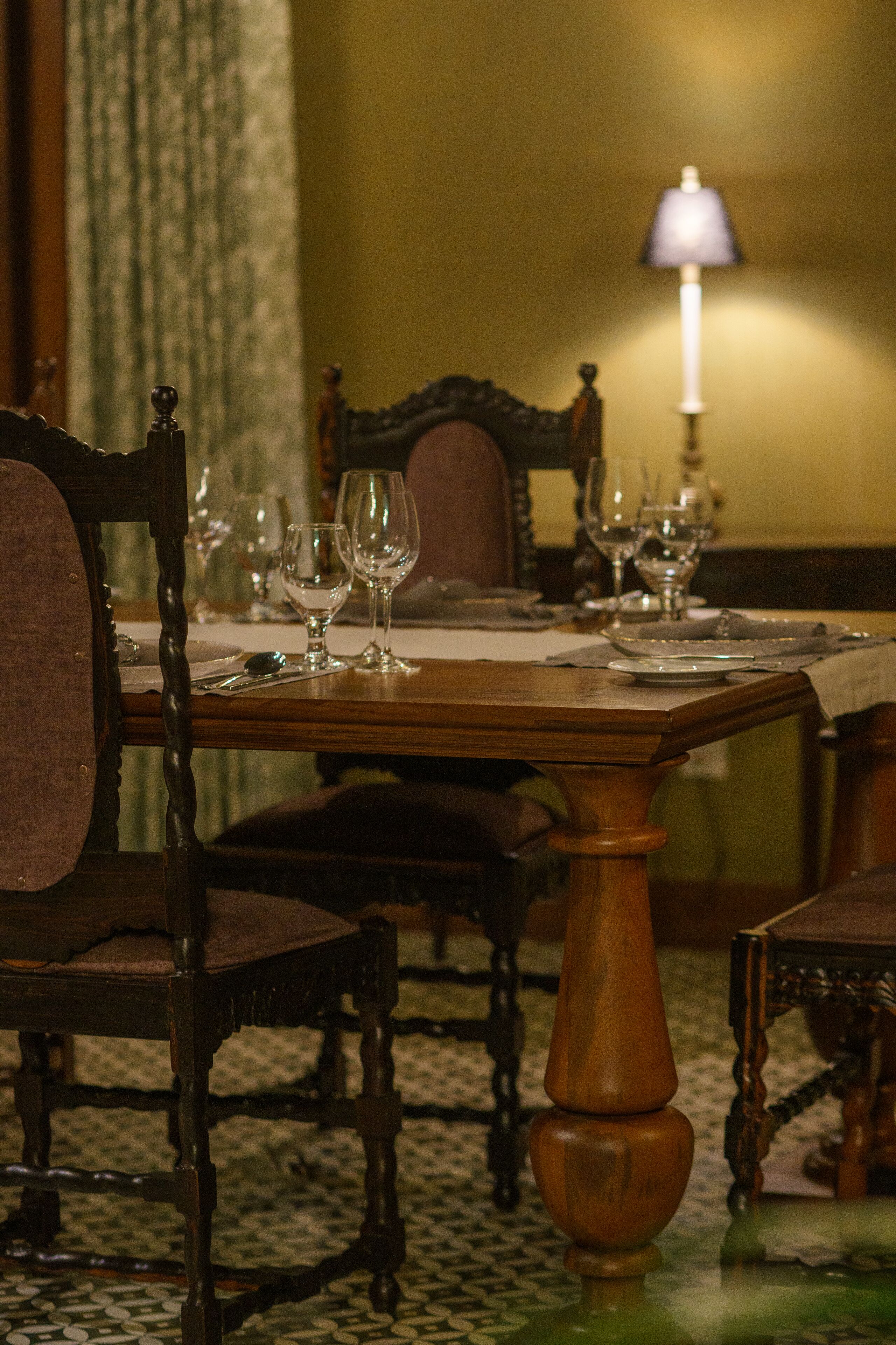 A dining table set with wine glasses and plates, surrounded by upholstered chairs.