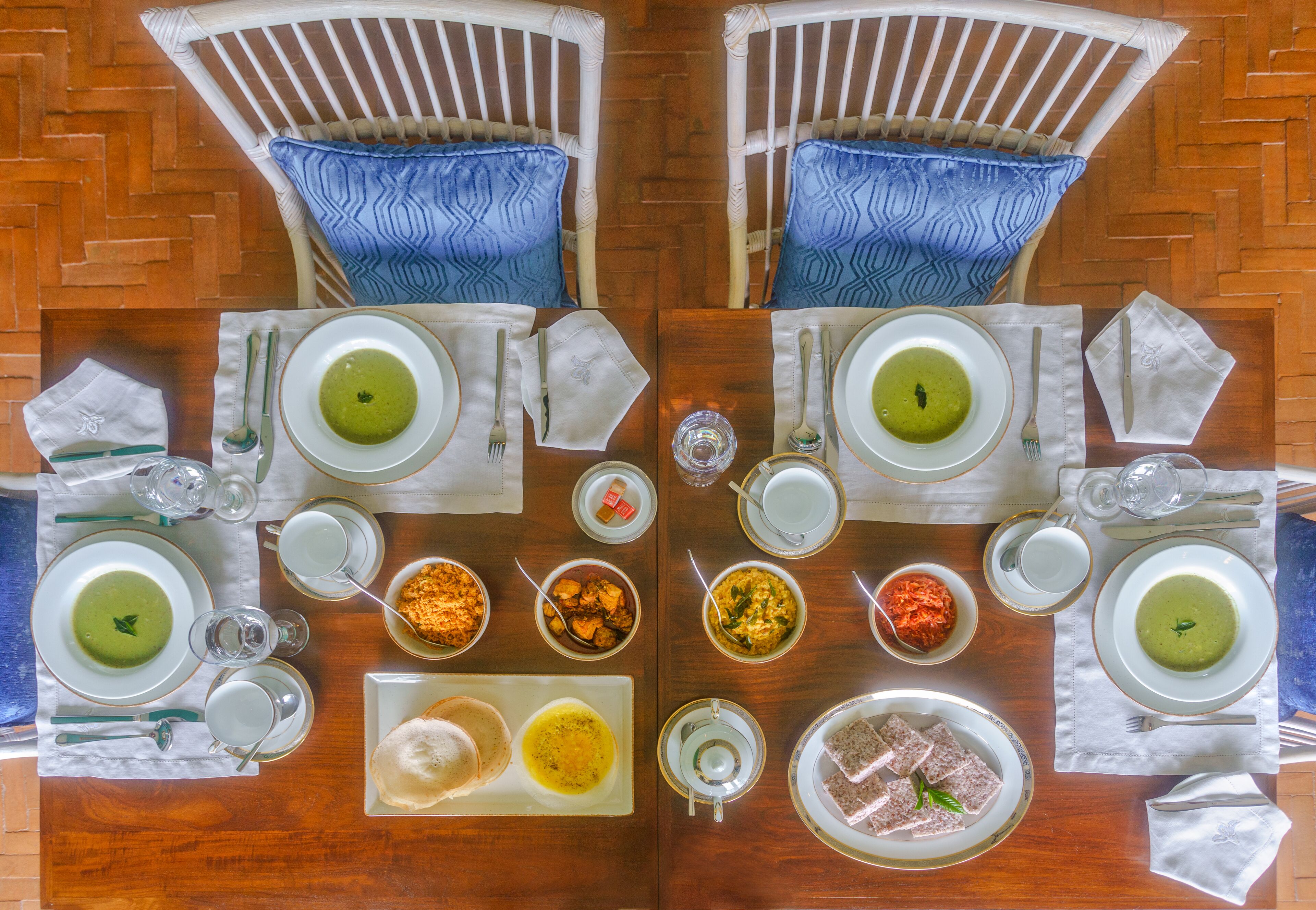 A dining table set for two with various dishes, including green soup and curry, arranged on white plates with gold rims.